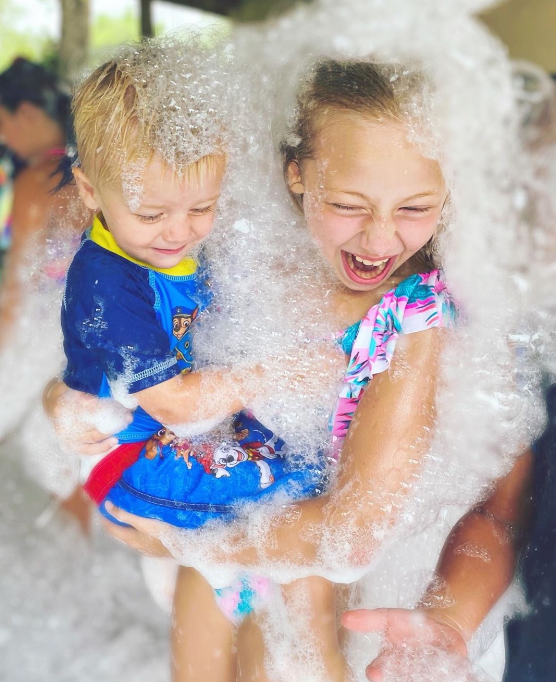 Two young siblings laughing together in a cascade of foam